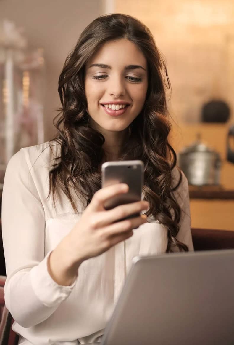 Femme avec smartphone et ordinateur Femme professionnelle souriante consultant son smartphone devant son ordinateur portable.